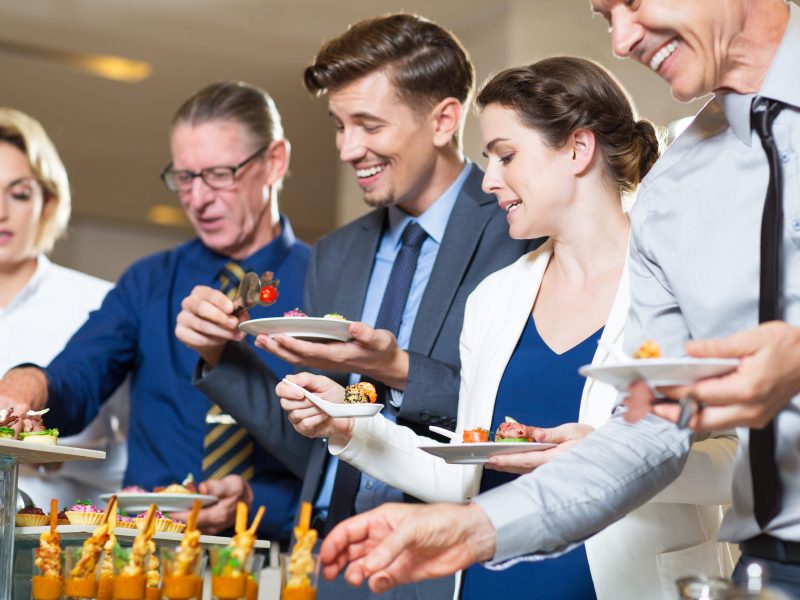 Group of five business people standing in buffet of restaurant and serving themselves with snacks. Catering concept